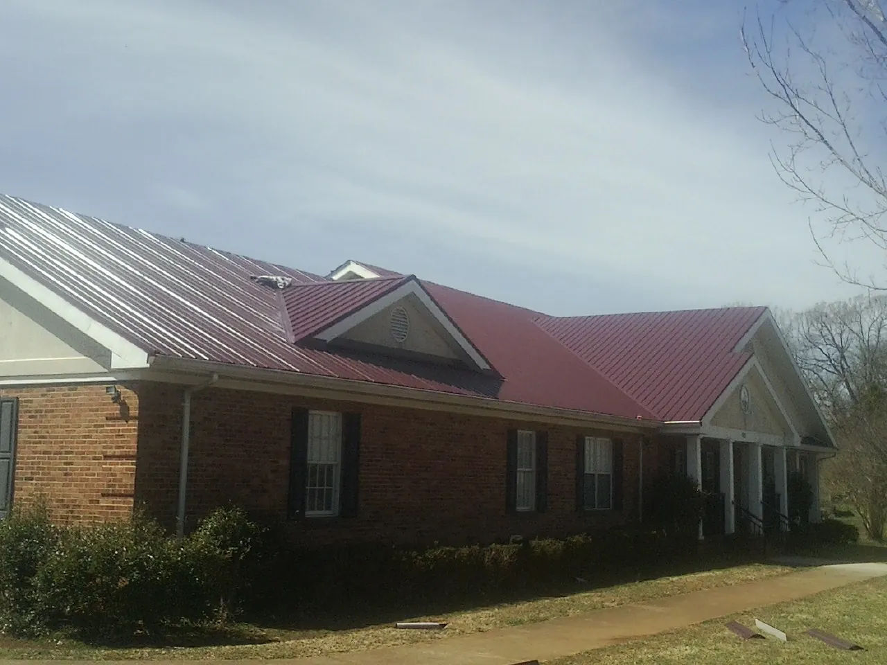 Red metal roof with gabled entries on a long brick building, from a Hail Damage Roof Repair job in Fairview