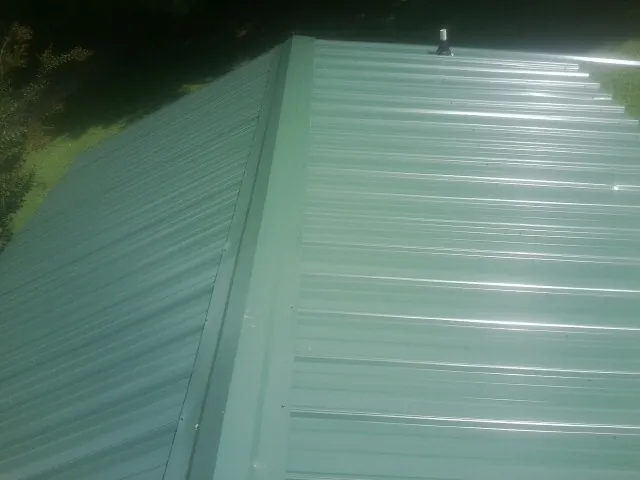 New green metal panels meeting at the ridge of a roof — Flat Roof Repair work by our crew in Fairview